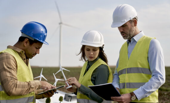 Team of caucasian and latin engineers standing on wind turbine field and discussing Team of caucasian and latin engineers standing on wind turbine field and discussing